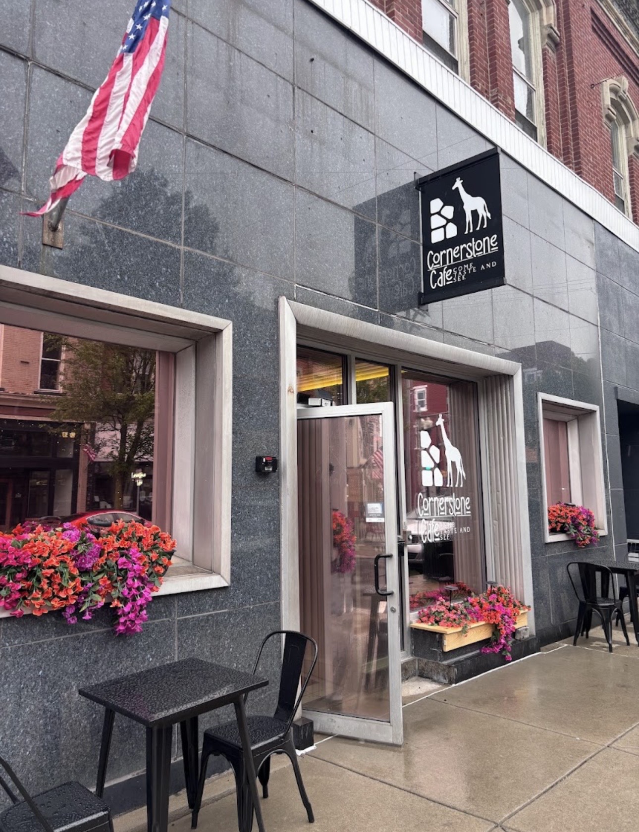 Cornerstone Café storefront at 107 E State Street, Sharon PA — black sign with giraffe logo and vibrant flower boxes